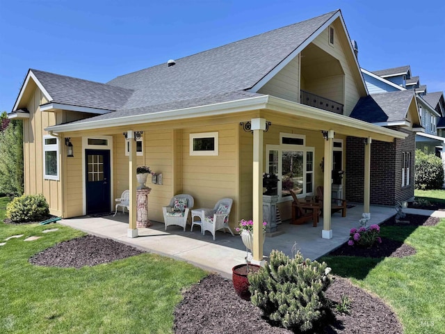 rear view of property with a yard, board and batten siding, a shingled roof, and a patio area
