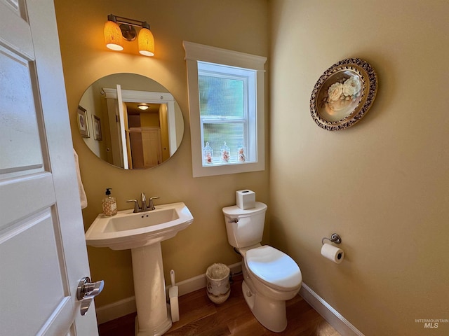 half bath featuring baseboards, wood finished floors, and toilet