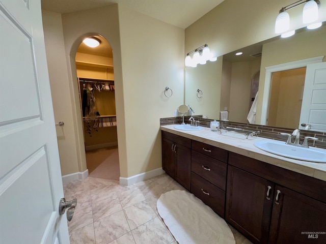 full bathroom featuring double vanity, a sink, baseboards, and a walk in closet