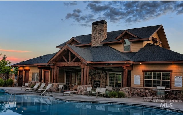 back of house featuring a community pool, a patio, and a chimney