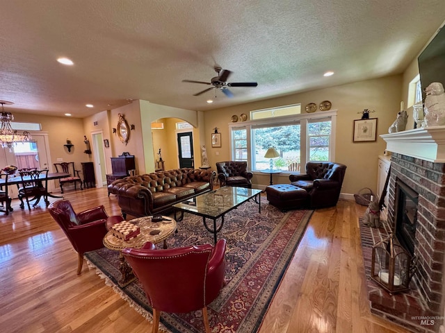 living area with arched walkways, a brick fireplace, light wood finished floors, and a textured ceiling