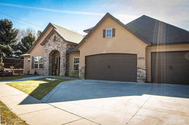 view of front of property with an attached garage, stone siding, a shingled roof, and stucco siding