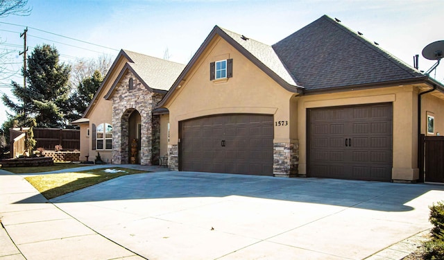 view of front of property featuring stone siding, fence, concrete driveway, and stucco siding