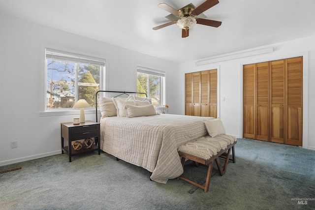 carpeted bedroom with baseboards, visible vents, two closets, and ceiling fan