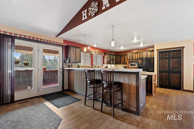 kitchen featuring light countertops, wood finished floors, visible vents, black refrigerator with ice dispenser, and a kitchen bar