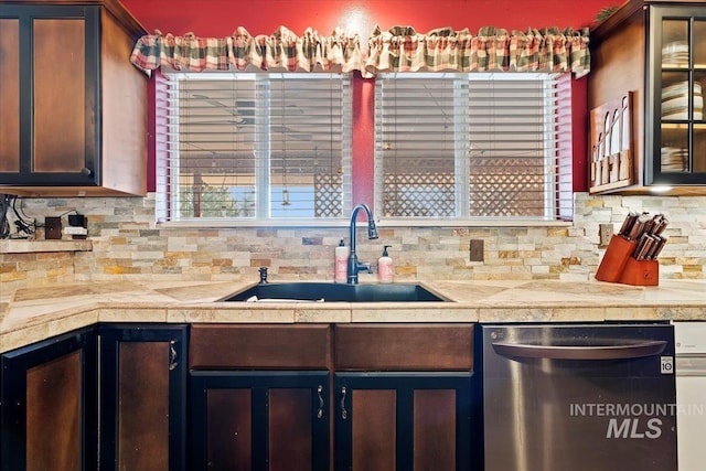 kitchen with decorative backsplash, stainless steel dishwasher, a sink, and glass insert cabinets