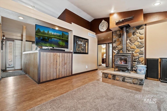 living room featuring vaulted ceiling, wood finished floors, a wood stove, visible vents, and baseboards