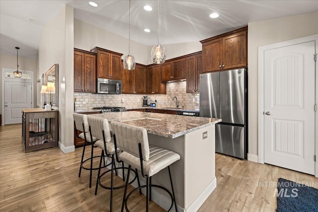 kitchen featuring stainless steel appliances, a sink, light stone counters, backsplash, and a breakfast bar area