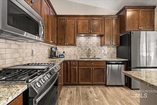 kitchen with appliances with stainless steel finishes, a sink, light stone countertops, tasteful backsplash, and lofted ceiling