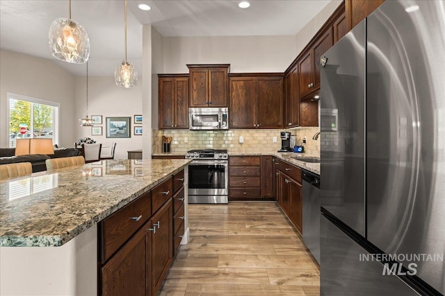 kitchen with appliances with stainless steel finishes, light wood-style flooring, light stone countertops, decorative backsplash, and pendant lighting