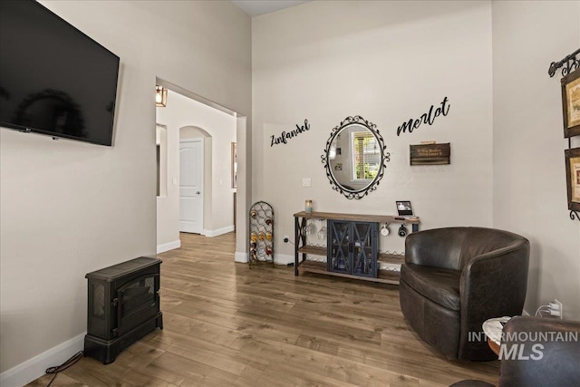 living area with arched walkways, a wood stove, wood finished floors, and baseboards
