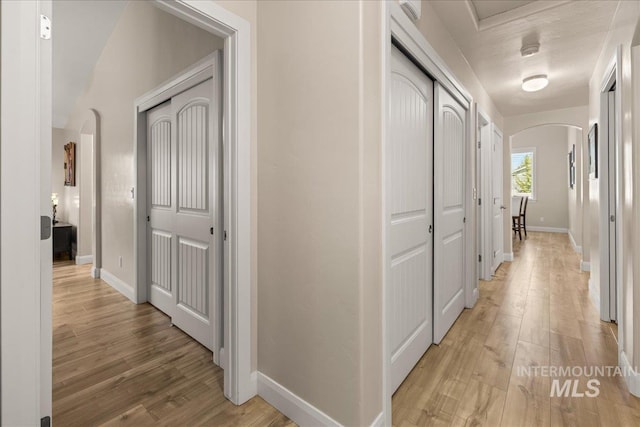 corridor featuring arched walkways, light wood-type flooring, and baseboards
