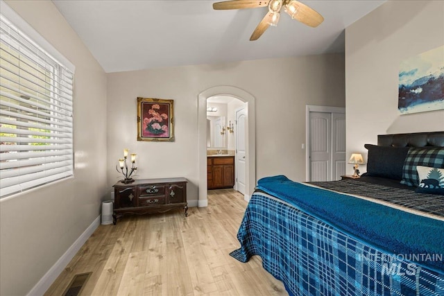 bedroom featuring arched walkways, light wood-style flooring, vaulted ceiling, baseboards, and connected bathroom