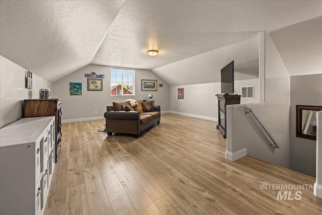 sitting room with an upstairs landing, light wood-type flooring, vaulted ceiling, a textured ceiling, and baseboards
