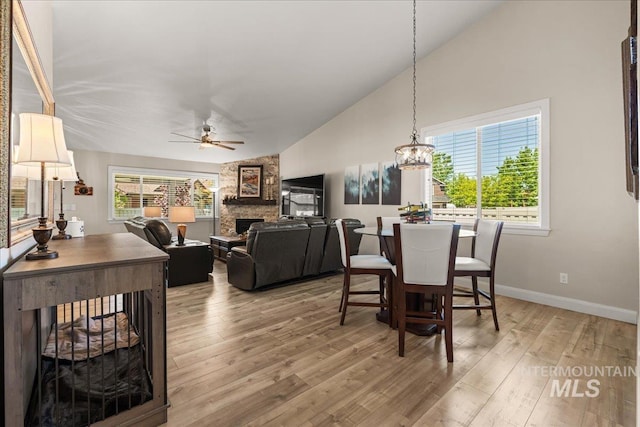 dining area with a stone fireplace, ceiling fan, baseboards, light wood-style flooring, and a chandelier