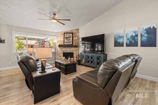 living area with vaulted ceiling, ceiling fan, baseboards, a stone fireplace, and light wood-style floors