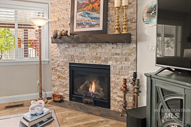 detailed view of wood finished floors, a stone fireplace, and baseboards