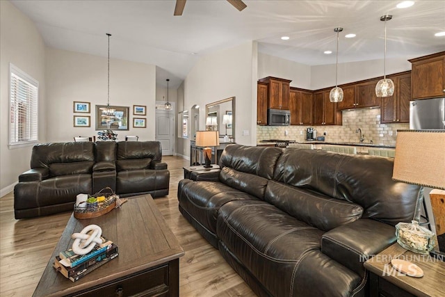 living area with baseboards, light wood-style flooring, a ceiling fan, high vaulted ceiling, and a chandelier