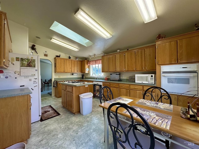kitchen featuring a sink, a kitchen island, lofted ceiling with skylight, white appliances, and brown cabinetry