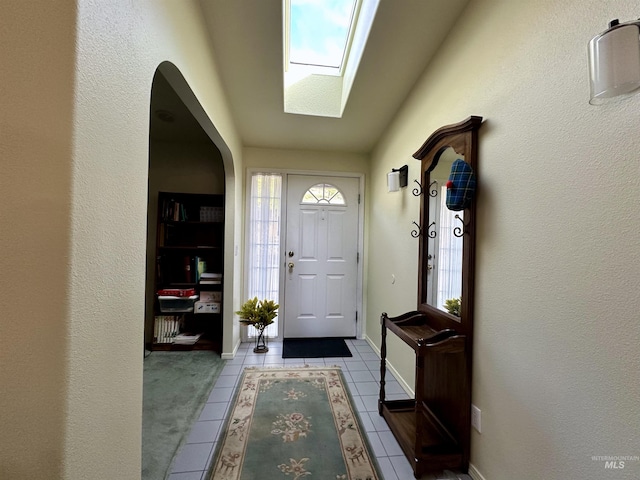 doorway to outside featuring plenty of natural light, tile patterned flooring, a skylight, and arched walkways