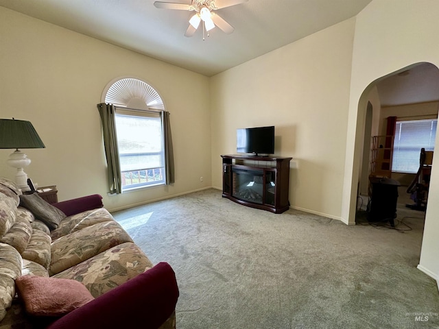 living area featuring lofted ceiling, ceiling fan, baseboards, arched walkways, and carpet