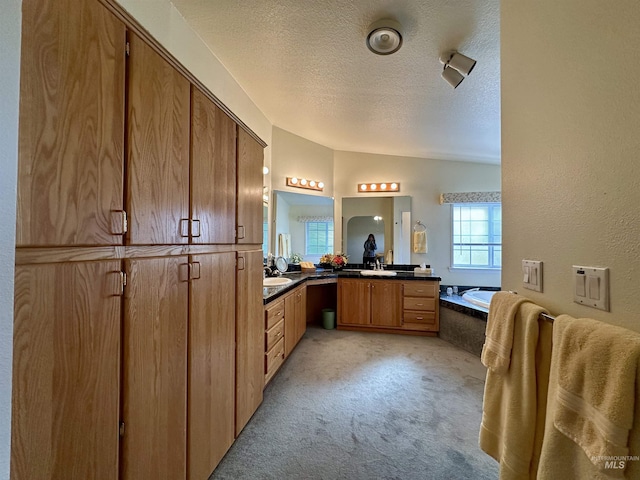 full bath with a garden tub, two vanities, vaulted ceiling, a sink, and a textured ceiling