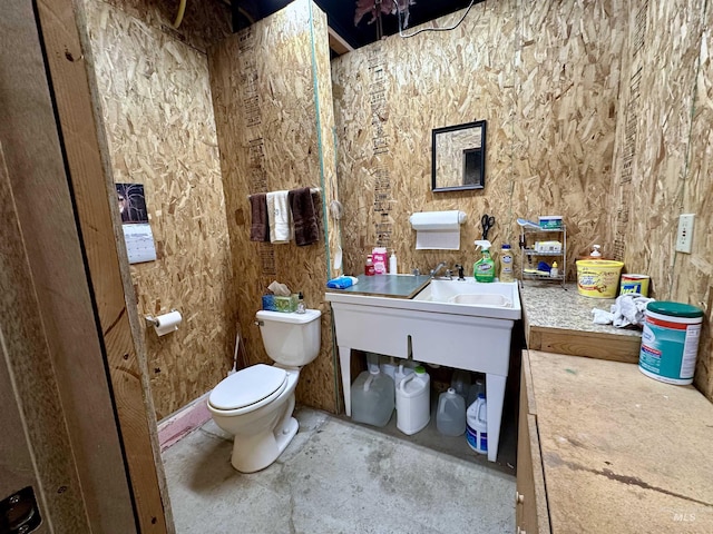 half bath with toilet, concrete floors, and a sink