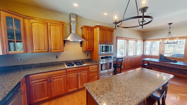 kitchen featuring pendant lighting, appliances with stainless steel finishes, wall chimney exhaust hood, a kitchen island, and a chandelier