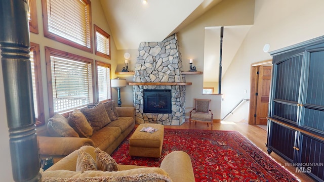 living room featuring a stone fireplace, high vaulted ceiling, and light hardwood / wood-style floors