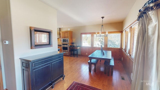 dining space featuring hardwood / wood-style flooring, wooden walls, and a chandelier