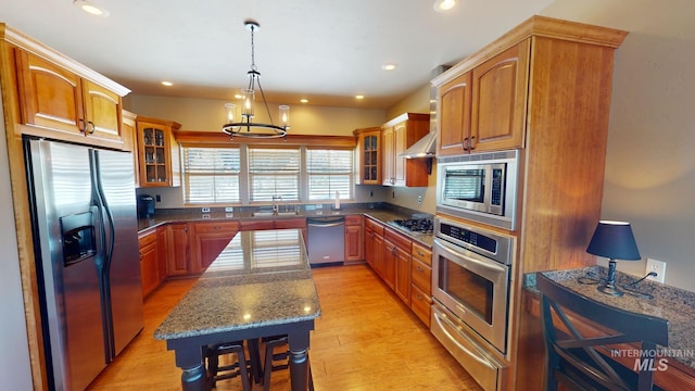 kitchen featuring a kitchen island, dark stone counters, hanging light fixtures, stainless steel appliances, and light wood-type flooring