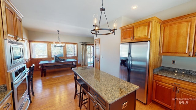 kitchen with an inviting chandelier, decorative light fixtures, a center island, stone counters, and stainless steel appliances