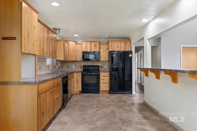 kitchen featuring dark countertops, backsplash, a sink, black appliances, and baseboards