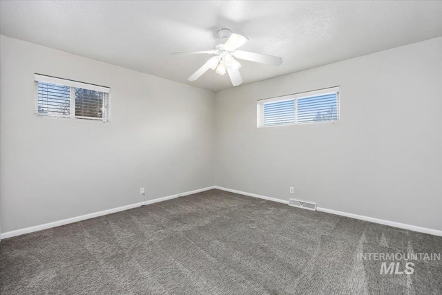 empty room featuring ceiling fan, dark colored carpet, visible vents, and baseboards