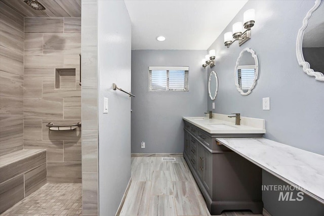 full bath featuring a sink, a tile shower, and double vanity