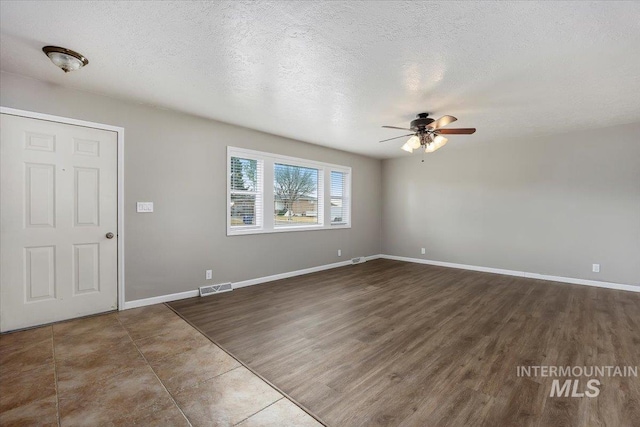 empty room featuring a textured ceiling, ceiling fan, wood finished floors, visible vents, and baseboards