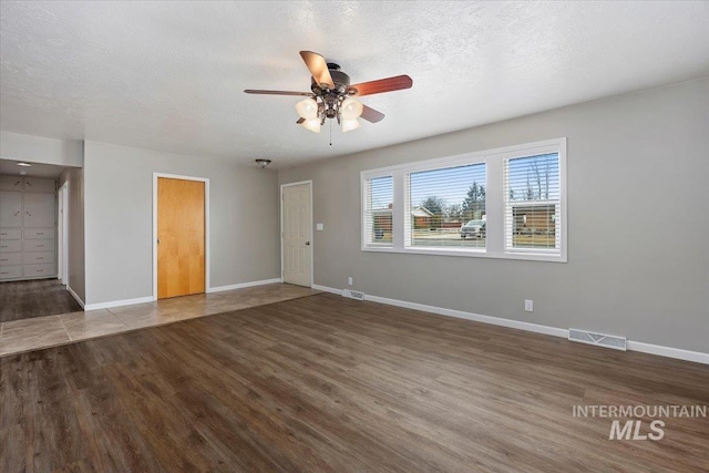 unfurnished living room featuring a textured ceiling, wood finished floors, a ceiling fan, visible vents, and baseboards