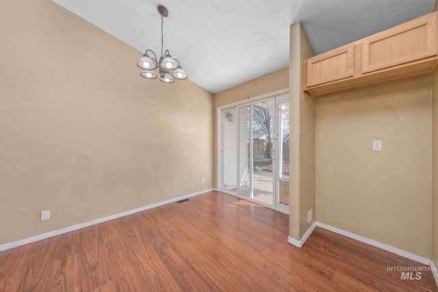 unfurnished dining area featuring baseboards, a notable chandelier, lofted ceiling, and dark wood-style floors