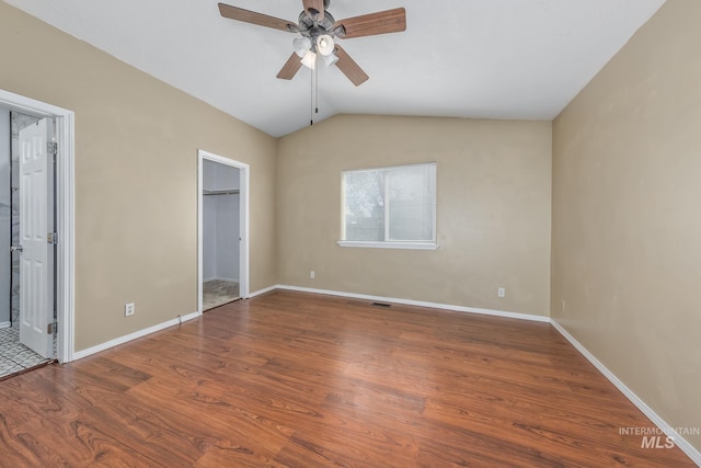 unfurnished bedroom with baseboards, a ceiling fan, a walk in closet, vaulted ceiling, and wood finished floors