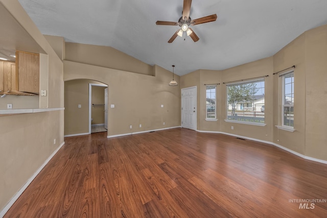 unfurnished living room with baseboards, vaulted ceiling, ceiling fan, arched walkways, and wood finished floors