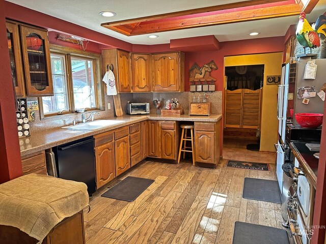 kitchen featuring a sink, light wood-style floors, black dishwasher, brown cabinets, and light countertops