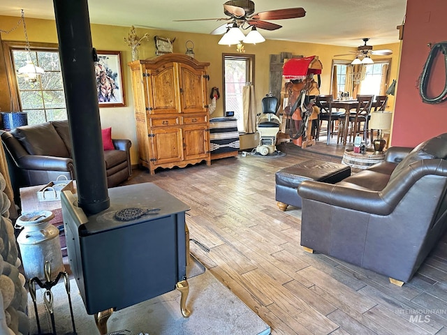 living room with ceiling fan, a wood stove, and wood finished floors