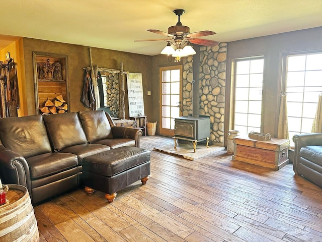 living room with a wood stove, ceiling fan, and light wood-style floors