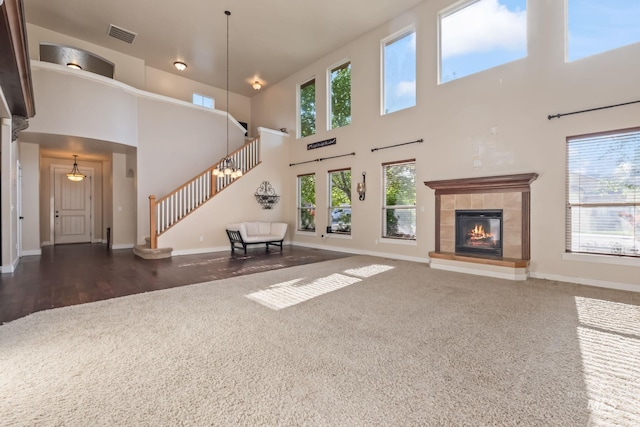 unfurnished living room featuring a towering ceiling, a tile fireplace, baseboards, carpet floors, and stairs