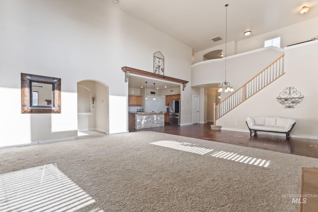 unfurnished living room with arched walkways, dark carpet, stairs, baseboards, and a towering ceiling