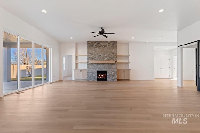 unfurnished living room featuring light wood-type flooring, ceiling fan, a wealth of natural light, and a fireplace