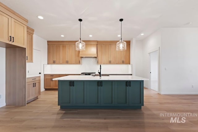 kitchen featuring custom exhaust hood, a center island with sink, decorative light fixtures, light wood-type flooring, and sink