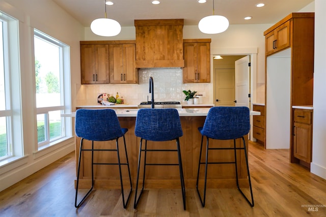 1038 E Fleetwood Ct, Boise, ID 83706 - kitchen featuring brown cabinets, backsplash, light countertops, light wood-type flooring, and a kitchen island with sink