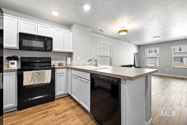 kitchen with a peninsula, a sink, white cabinets, open floor plan, and black appliances