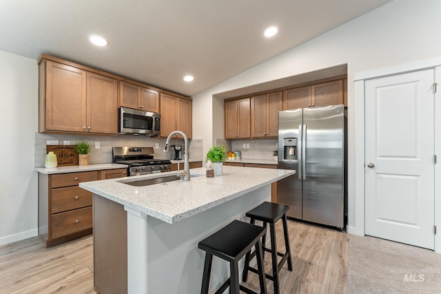 kitchen with a kitchen breakfast bar, backsplash, light wood-type flooring, a sink, and stainless steel appliances